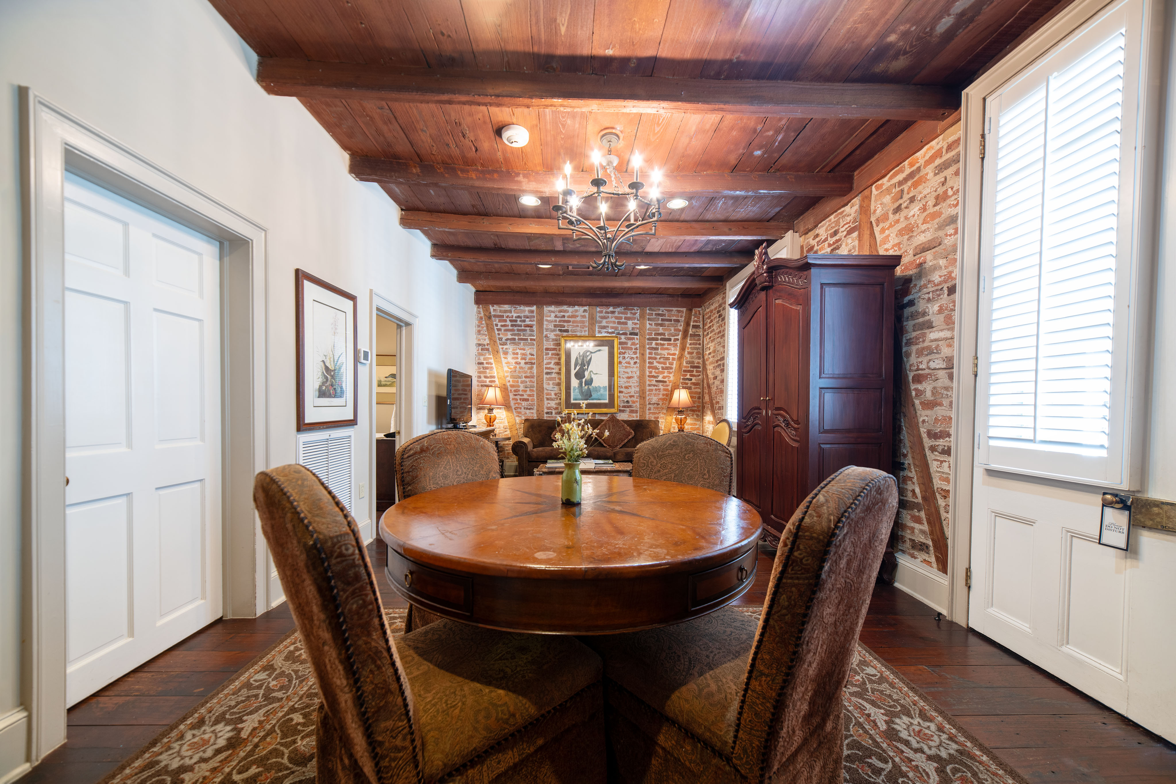 A dining area with a round table and chairs, brick wall, wood ceiling, and chandelier.