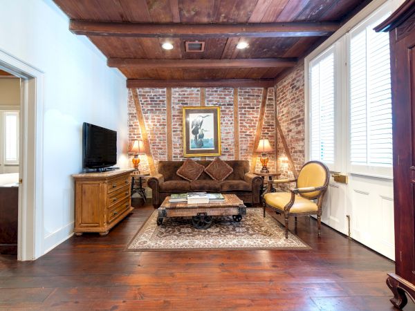 A cozy living room with brick walls, a couch, coffee table, TV, and armchair; decorated with a painting, lamps, and wooden furniture.