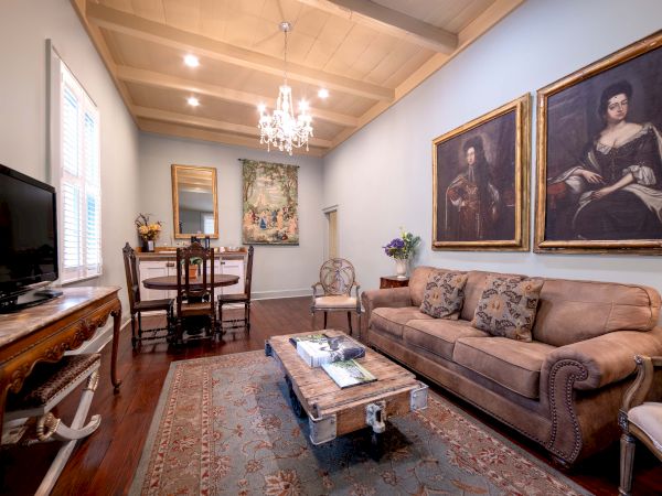 A cozy living room with a chandelier, classic paintings, a sofa, a coffee table, and a dining area in the background.