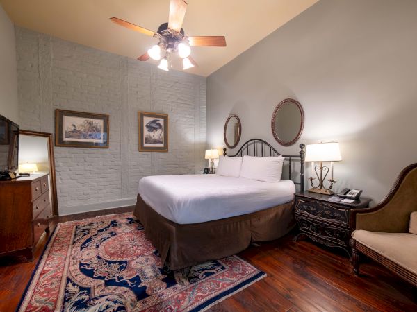 A cozy bedroom with a large bed, two lamps, a ceiling fan, and a TV. Decor includes two mirrors and framed pictures on the wall.
