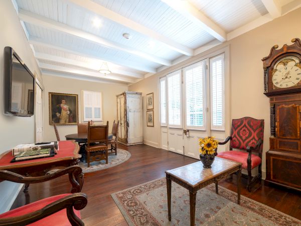 A traditional room with wooden floors, a grandfather clock, red-upholstered chairs, a painting, and a table with sunflowers.