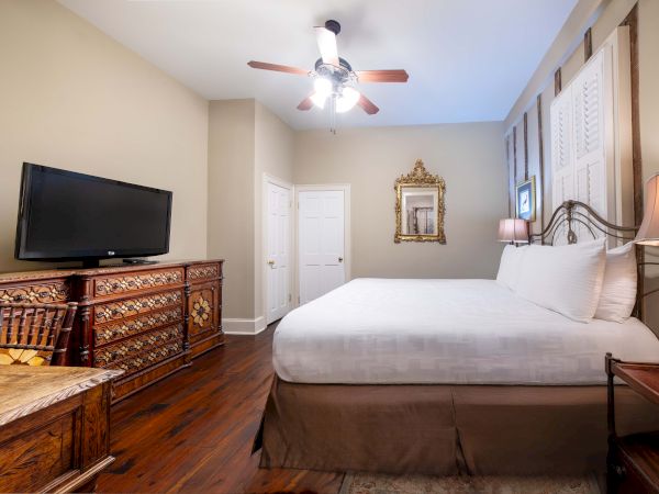 A cozy bedroom with a large bed, ornate furniture, a TV, a ceiling fan, and a decorative mirror on the wall complete the setting.