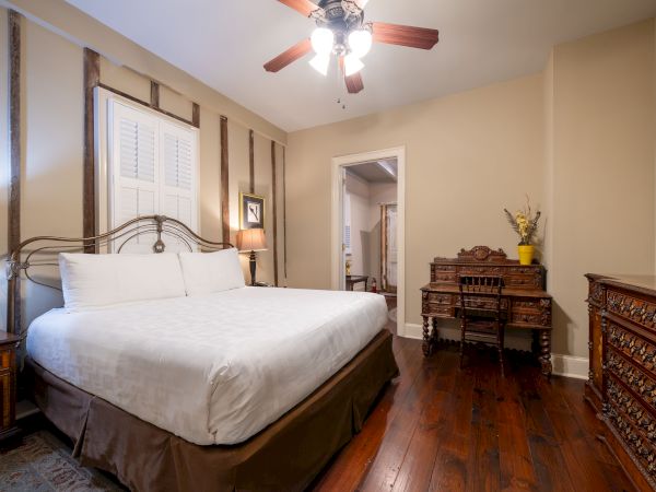 A cozy bedroom featuring a large bed, wooden furniture, decorative items, ceiling fan, and a TV on a dresser completes the scene.