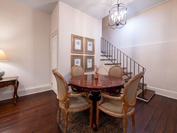 A cozy dining area with a round table, four chairs, and a staircase. Wall art and a lamp on a side table complete the decor.