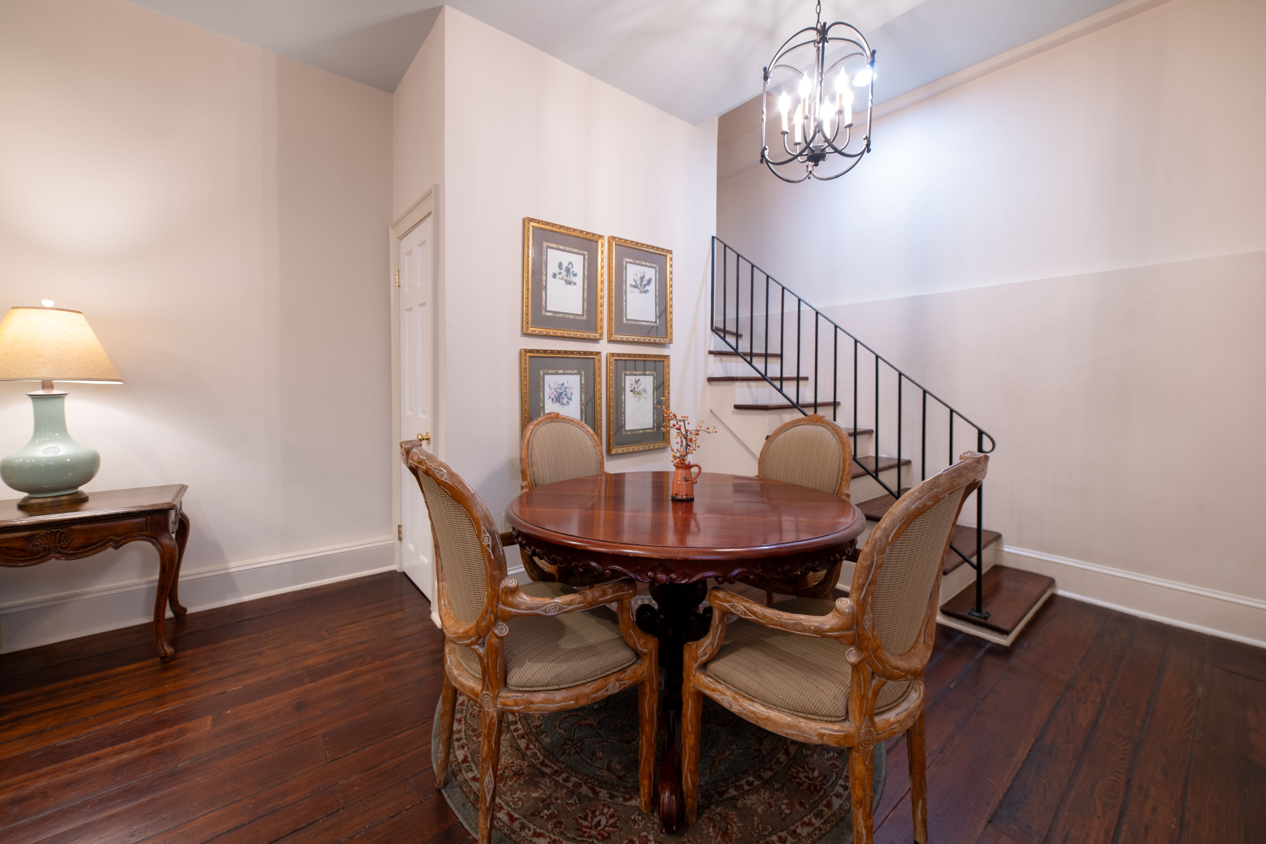 A dining area with a round table, chairs, a staircase, and a chandelier.