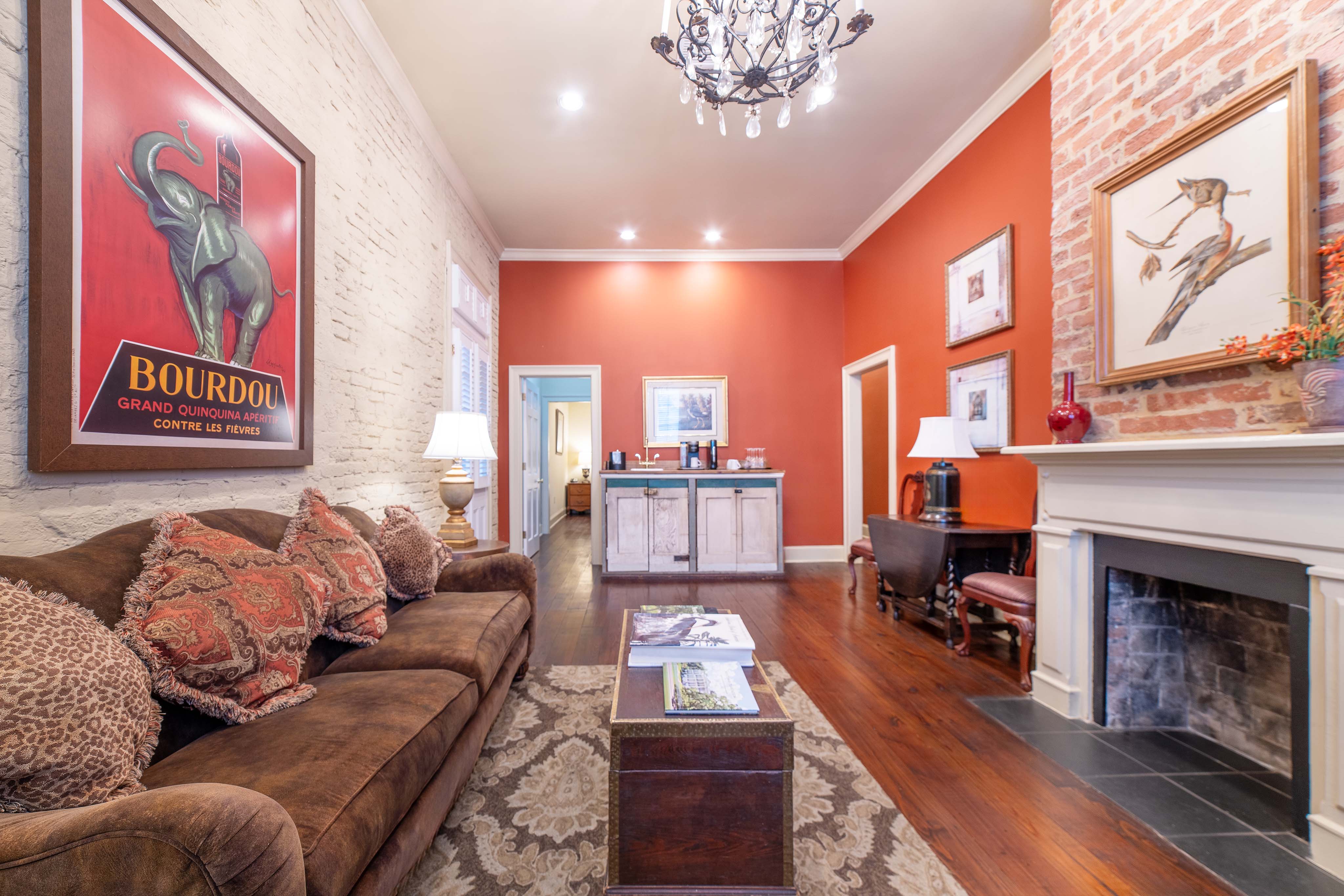 A wide view of a stylish living room with a brown sofa, chandelier, and brick accent wall.