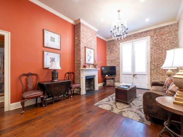 A cozy living room with a brick wall, fireplace, wooden furniture, chandelier, and TV on a stand; styled in warm tones.