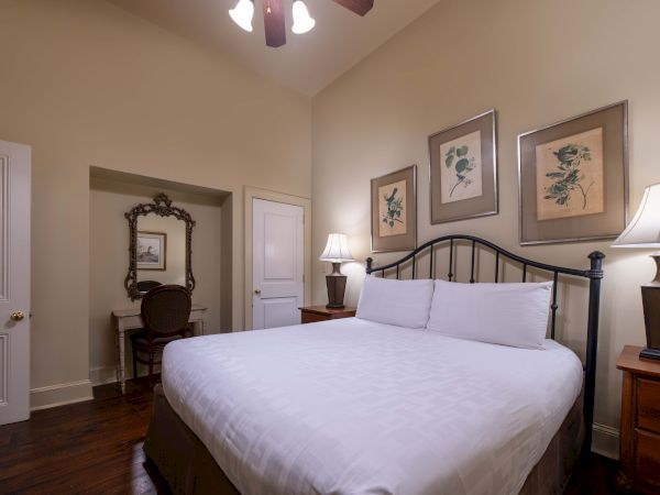 A cozy bedroom with a large bed, two lamps, framed art above, and a small vanity with a chair in the corner of the room.