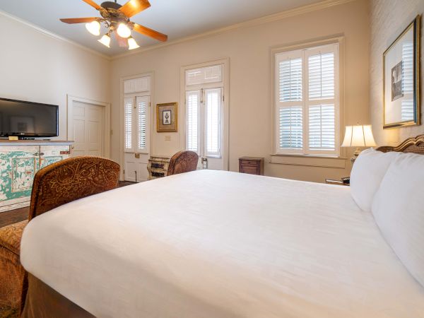 A cozy bedroom with a large bed, TV on a cabinet, ceiling fan, and a window with shutters, creating a warm and inviting atmosphere.