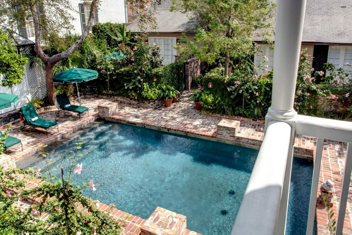 A swimming pool with lounge chairs and umbrella surrounded by trees and brick pavers