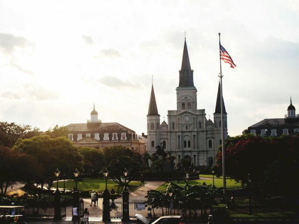 A cathedral with three spires and an American flag in front, surrounded by greenery and buildings in the background.<|vq_61|>