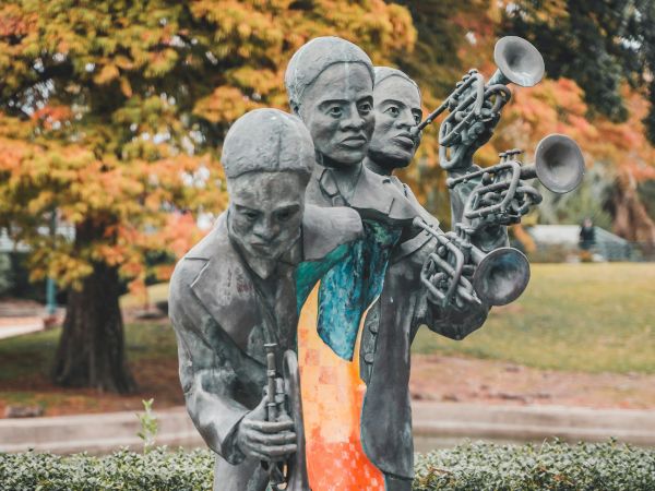 A sculpture of three musicians with trumpets, set outdoors, with autumn trees in the background, featuring a colorful central section.
