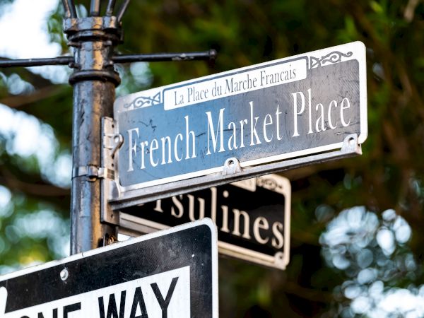 Street signs for French Market Place and one-way direction, with trees in the background.