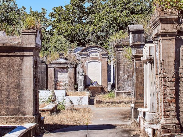 An outdoor cemetery scene with above-ground tombs, weathered stone, and vegetation under a clear blue sky.