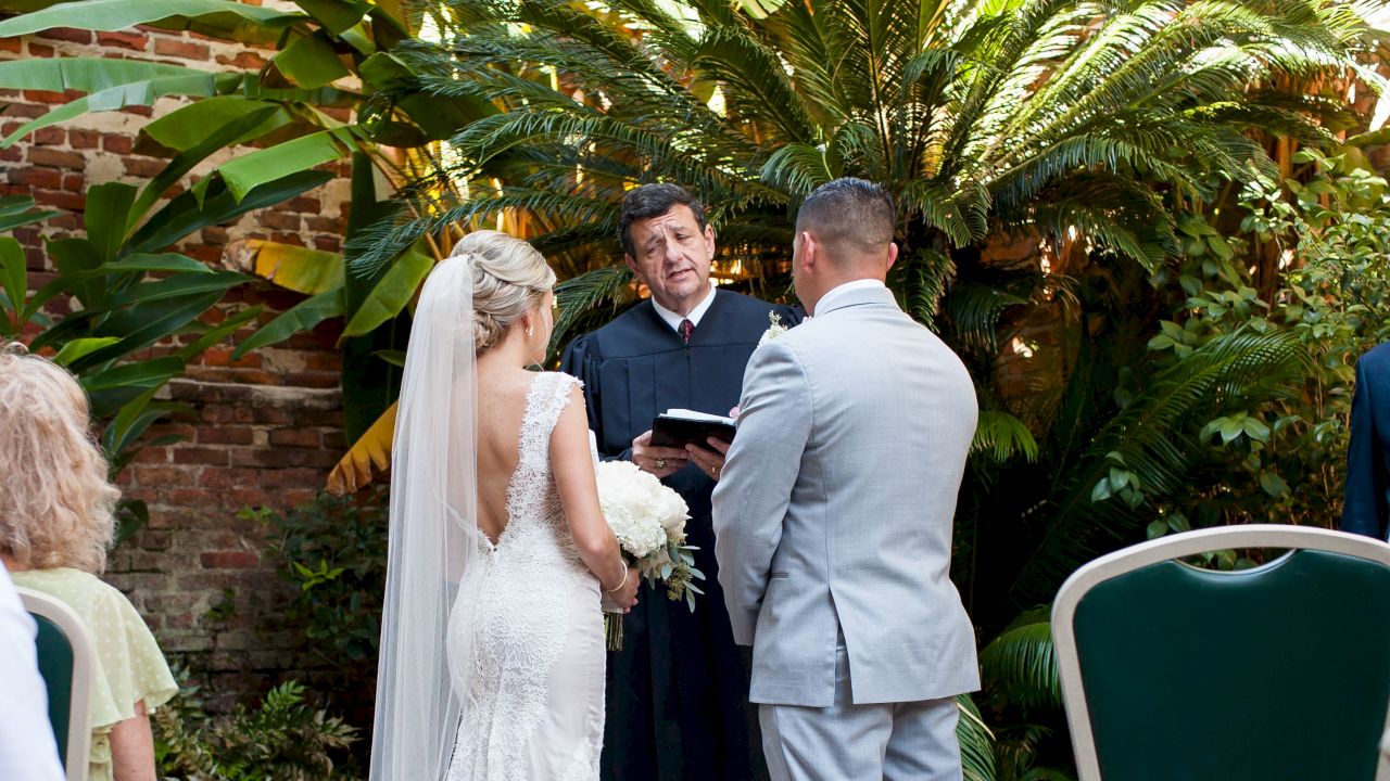 A wedding ceremony taking place outdoors with a bride, groom, and officiant.