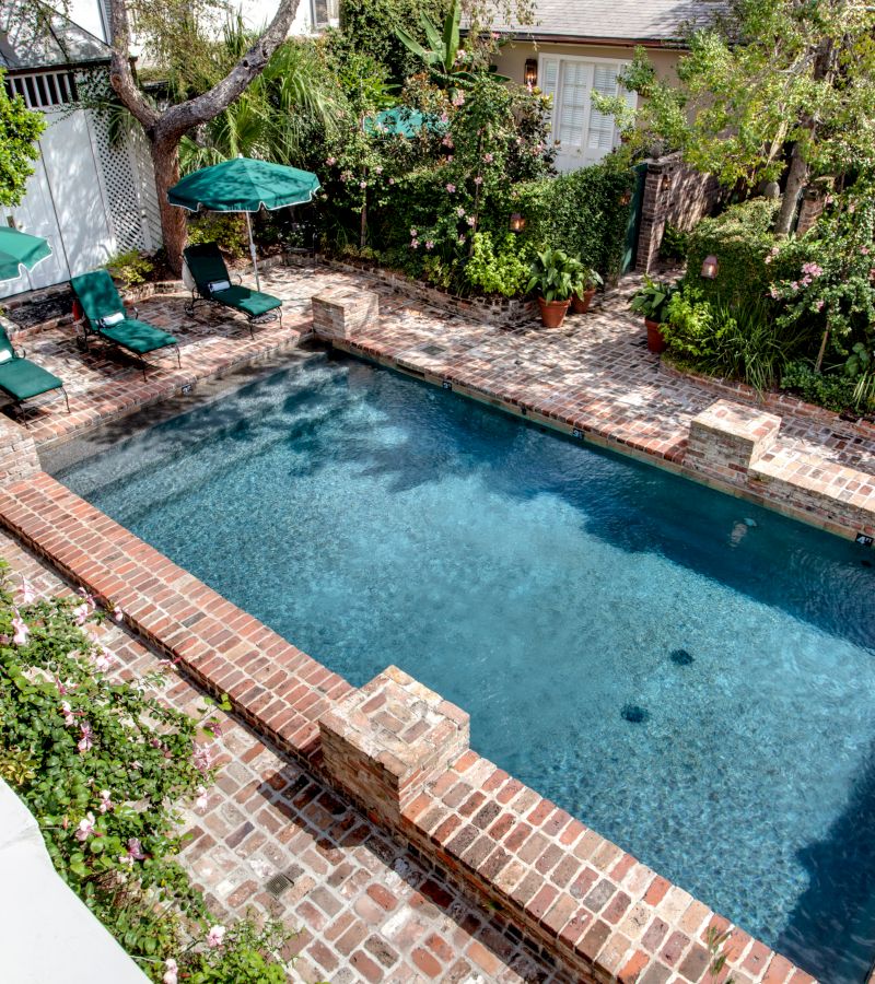 A rectangular pool with a brick deck, surrounded by greenery and lounge chairs.