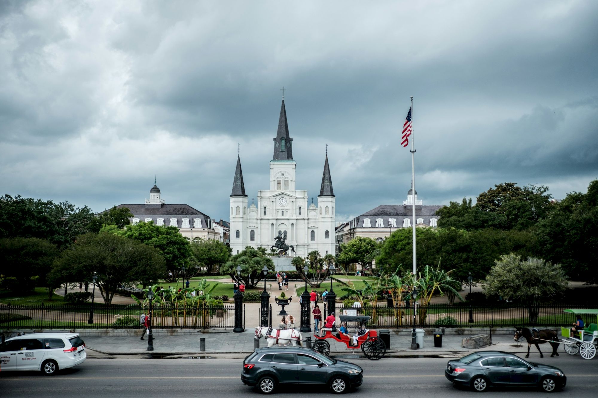 The image shows St. Louis Cathedral in New Orleans, with cars and a horse-drawn carriage in the foreground on a cloudy day.