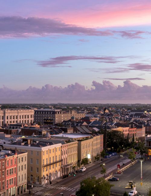 A scenic view of a historic town at dusk, with colorful buildings, a church spire, and a calm sky painted in pink and blue hues.