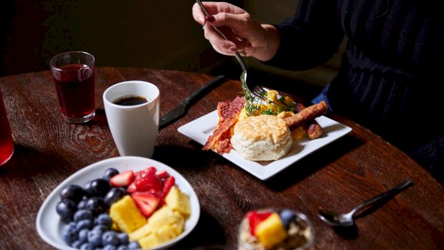 A breakfast table with a plate of fruit, a plate of food, and a cup of coffee.