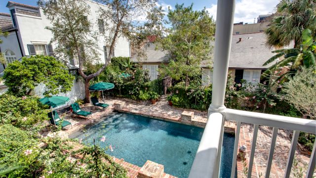 A pool with lounge chairs and umbrellas surrounded by trees and a balcony.