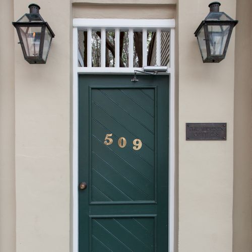 A green door marked with the number 509 is set in a beige wall, flanked by two lanterns, with trees visible above.