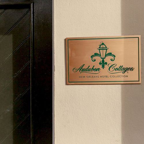 A plaque with "Audubon Cottages" and "New Orleans Hotel Collection" is mounted on a wall next to a dark-colored door.