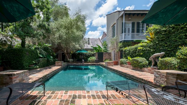 A swimming pool with lounge chairs and umbrellas surrounded by gardens and a building in the background.