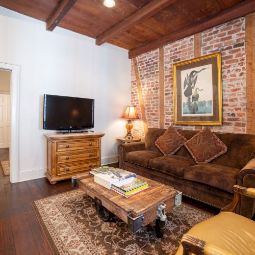 A cozy living room with exposed brick, a brown couch, two lamps, a TV on a wooden stand, and a coffee table on a rug.