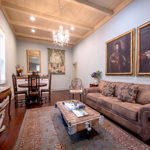 A cozy living room with a chandelier, paintings, a couch, a TV, and a small dining table, all in a classically styled space.
