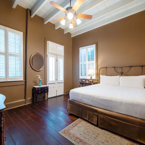 A cozy bedroom with a king-sized bed, wooden flooring, brown walls, a ceiling fan, and shuttered windows enhances the room’s warmth.