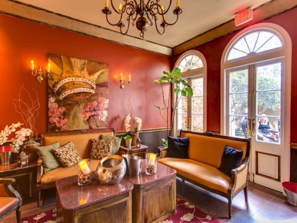 A cozy, elegant living room with warm red walls, a chandelier, leather sofa, plants, and a door to the outside. Ensure it ends with a period.