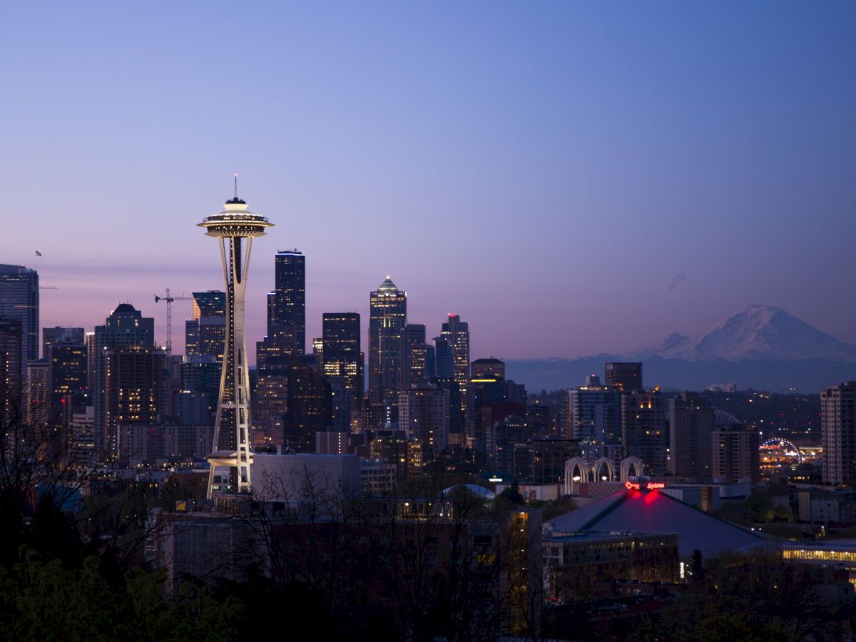 The image shows the Seattle skyline at dusk with the Space Needle prominently visible and Mount Rainier in the background under a twilight sky.